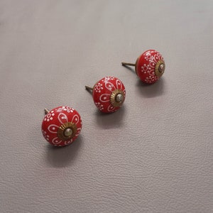 May include: Three red ceramic knobs with white floral designs. The knobs have a brass screw on the back.
