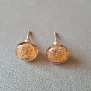 Könnte beinhalten: Zwei amberfarbene Glas-Schrankknöpfe mit einem silbernen Metallsockel. Das Glas hat eine blasige Textur.