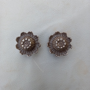 May include: Two silver-toned metal flower-shaped buttons with a raised center and a textured design.