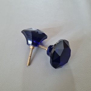 May include: Two blue glass cabinet knobs with a faceted diamond shape and gold metal screws.
