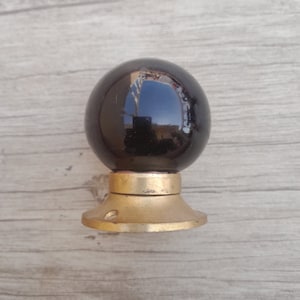 May include: A black ceramic door knob with a gold metal base. The knob is round and has a smooth, glossy finish.