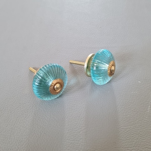 May include: Two aqua blue glass cabinet knobs with gold accents. The knobs have a fluted design and are attached to a metal screw.