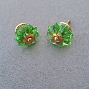 Könnte beinhalten: Zwei grüne Glas-Schrankknöpfe mit goldenen Metallakzenten. Die Knöpfe haben ein geriffeltes Design und sind perfekt, um jedem Zuhause einen Hauch von Vintage-Charme zu verleihen.