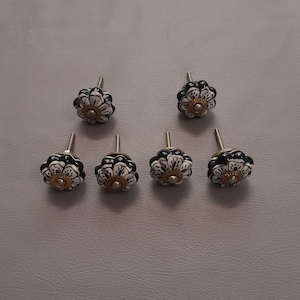 Peut inclure: Six boutons de tiroir en céramique noir et blanc avec un motif floral. Chaque bouton a un centre doré et une vis argentée.