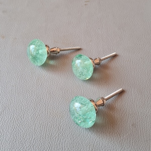 Peut inclure: Trois boutons de cabinet en verre vert avec des bases en métal argenté. Les boutons ont une finition texturée et mouchetée.