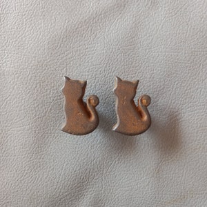 May include: Two rusty brown metal cat-shaped door knobs.