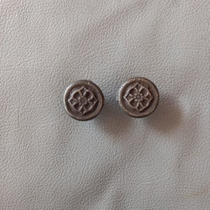 Puede incluir: Dos pequeños pomos redondos de metal marrón oscuro con un diseño floral decorativo.