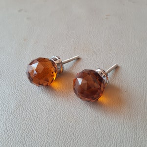Könnte beinhalten: Zwei amberfarbene Glas-Schrankknöpfe mit facettiertem Design und silbernen Metallstielen.