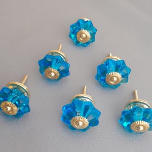 Könnte beinhalten: Sechs blaue Glas-Schrankknöpfe mit goldenen Metallakzenten. Die Knöpfe haben ein blumenartiges Design.