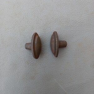 May include: Two rusty metal knobs with a rounded top and a short stem. The knobs are similar in size and shape.