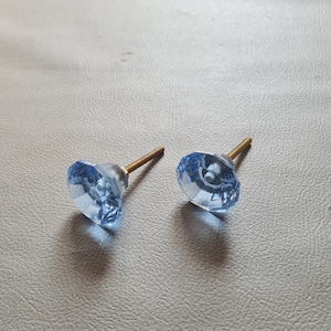 Puede incluir: Dos pomos de armario de cristal azul con un tornillo de latón. Los pomos tienen un diseño facetado.