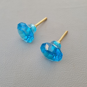 May include: Two blue glass cabinet knobs with gold metal screws. The knobs are faceted and have a geometric shape.