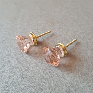 May include: Two pink glass cabinet knobs with gold metal bases and screws. The knobs are faceted and have a geometric shape.