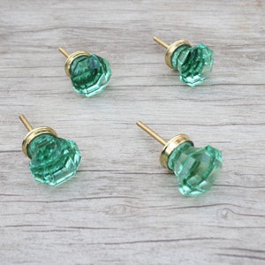 May include: Four green glass cabinet knobs with gold metal bases. The knobs have a faceted design.
