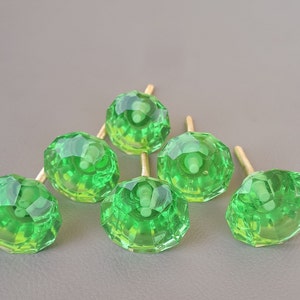 Puede incluir: Seis pomos de armario de vidrio verde con un diseño facetado y tornillos de metal dorado.