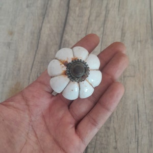 May include: White ceramic cabinet knob with a flower shape and a rusty metal center.