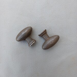 May include: Two antique metal door knobs with a brown finish. The knobs are oval shaped with a raised center and a small round knob on the side.