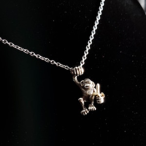 May include: A silver chain necklace with a silver monkey charm holding a gold banana. The monkey is sitting on its hind legs and has a detailed face.