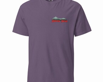 May include: Grape-colored t-shirt with a mountain and forest graphic. The graphic includes the text "Ambrosia Hollow" in red. The shirt is a short-sleeved crew neck.
