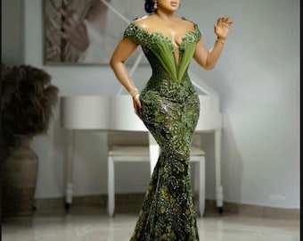 May include: A woman wearing a green, beaded, mermaid-style gown with a plunging neckline and a sheer overlay. The gown has a fitted bodice and a flowing skirt.