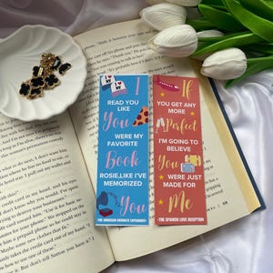 Puede incluir: Dos marcadores de libros coloridos con texto e ilustraciones. El marcador azul dice "Read you like you were my favorite book, Rosie, like I've memorized you." El marcador rojo dice "If you get any more perfect, I'm going to believe you were just made for me."