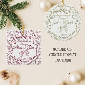 A square white ceramic ornament with red text and illustrations is next to a round white ceramic ornament with gold text and illustrations, both with gold hanging strings, on a white surface with pine branches and ornaments.