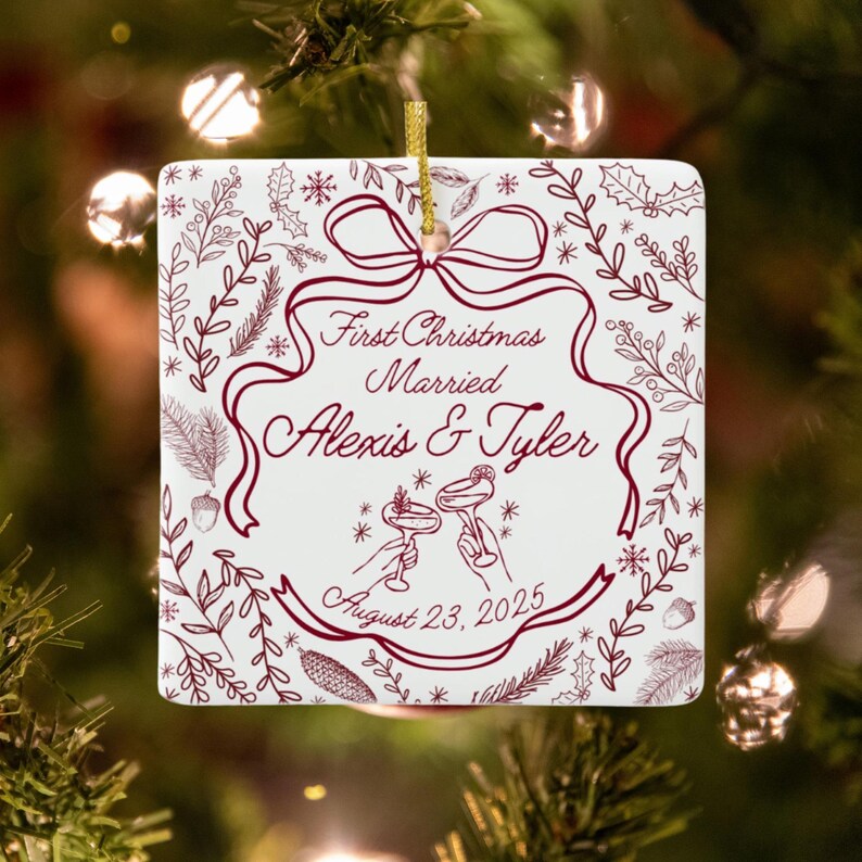A square, white ceramic ornament with red text and illustrations, reading "First Christmas Married Alexis & Tyler August 23, 2025," hangs on a Christmas tree with blurred lights.