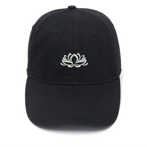 Könnte beinhalten: Eine schwarze Baseballkappe mit einem weißen, gestickten Lotusblüten-Design.