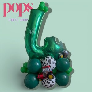 May include: A green number 4 balloon with the name "Will" written on it, surrounded by green, white, and black balloons. A red and yellow tractor balloon is also included. The image has the text "pops PARTY SHOP" in pink.