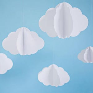May include: White paper cloud decorations suspended against a light blue backdrop. The clouds are three-dimensional, with layered construction for a fluffy look. Suitable for nursery or party decoration.