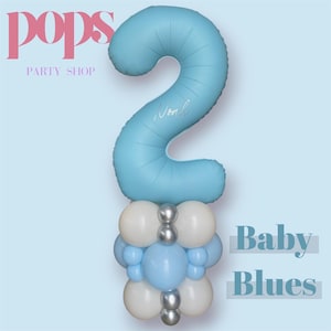 May include: A pale blue number 2 balloon with the name "Noah" in cursive, above a cluster of white, silver, and light blue balloons. The words "Baby Blues" are displayed on the right. The logo "Pops Party Shop" is in the upper left corner.