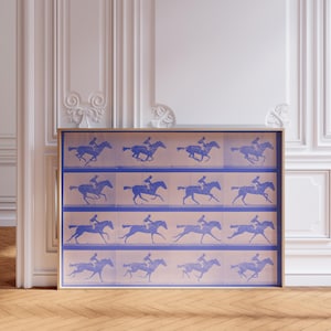 K&ouml;nnte beinhalten: Ein gerahmter Druck einer blauen Silhouette eines Pferdes und Reiters in einer Reihe von Posen, die einen Animationseffekt erzeugen. Der Druck ist auf einem hellrosa Hintergrund.