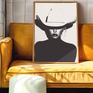 May include: Black and white photograph of a woman wearing a large white cowboy hat. The woman is looking directly at the camera. The background is a white wall.