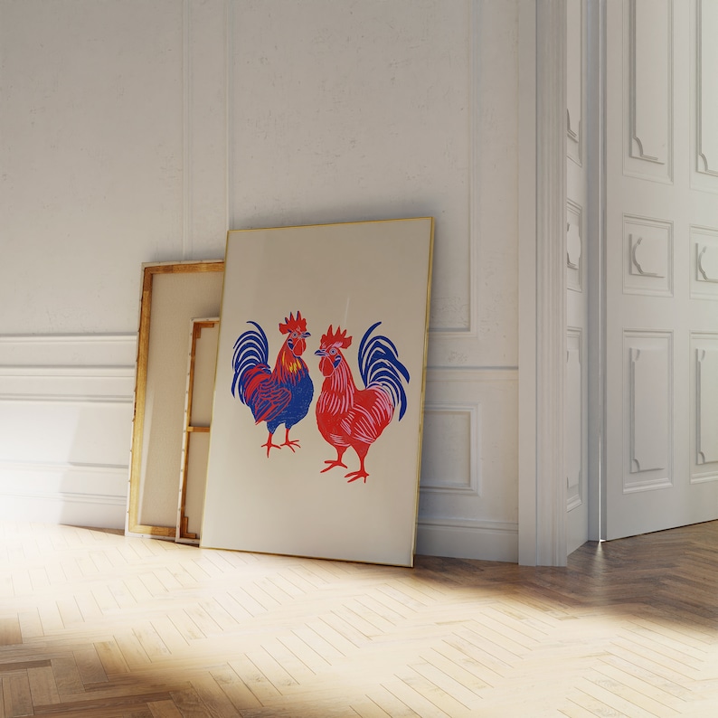 Op de afbeelding: Een ingelijste print van twee rode en blauwe hanen met zwarte contouren. De hanen staan ​​tegenover elkaar en hebben hun vleugels uitgespreid. De print is op een witte achtergrond en is ingelijst in een gouden lijst.