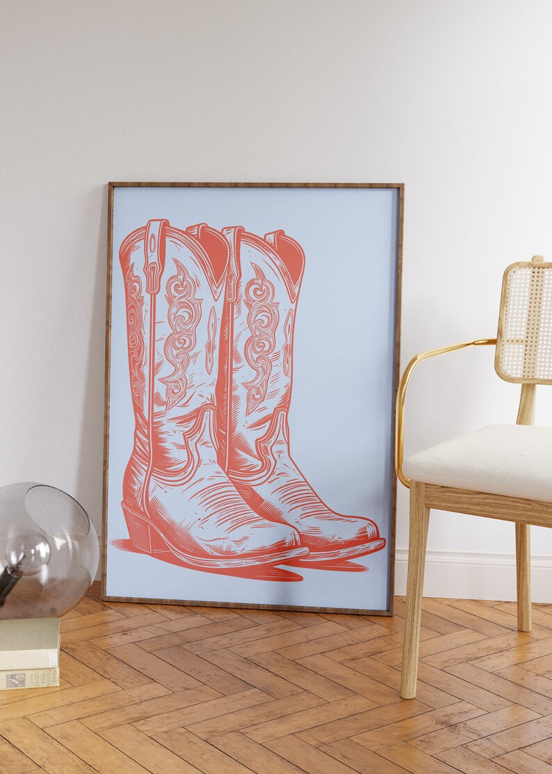 May include: A framed print of a pair of coral-colored cowboy boots on a light blue background.