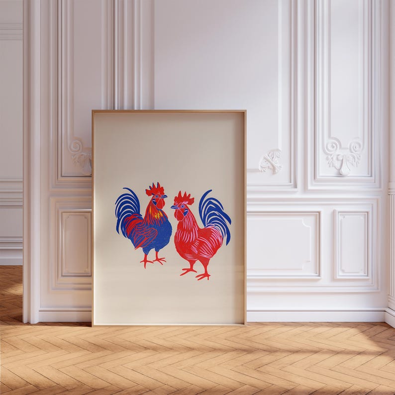 Op de afbeelding: Een ingelijst afdruk van twee hanen, een rood en een blauw, op een cr&egrave;mekleurige achtergrond.