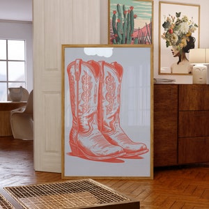 May include: A framed print of two red cowboy boots with intricate designs on a light blue background.