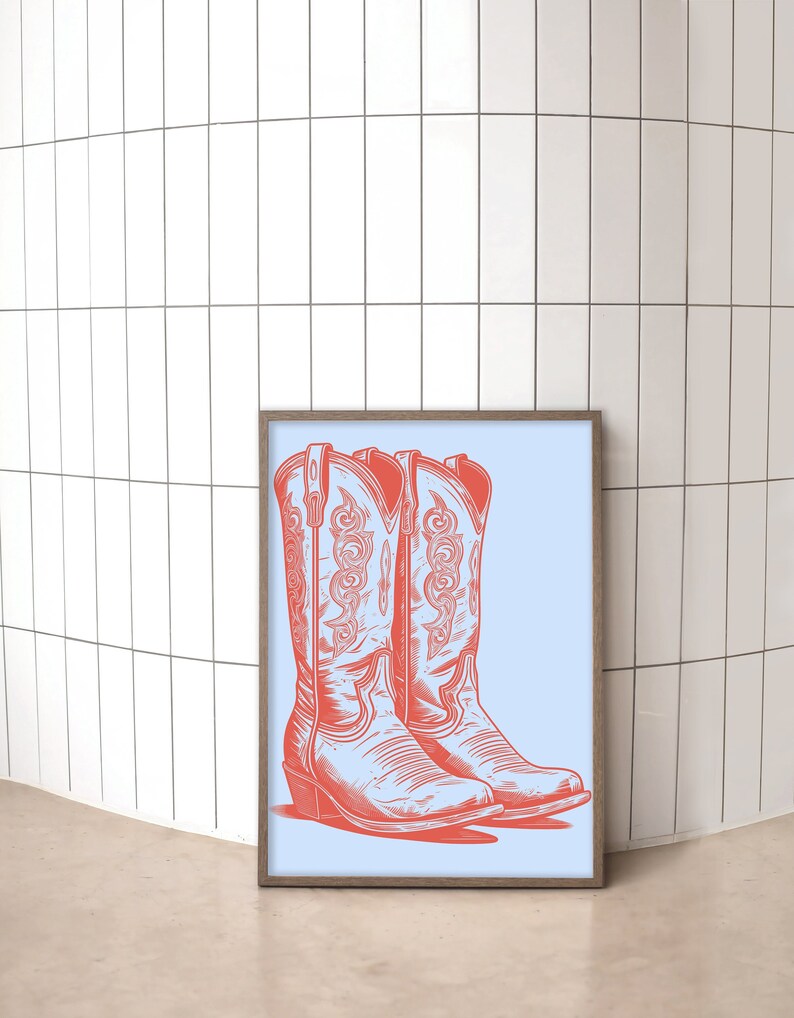 May include: A framed print of a pair of red cowboy boots on a light blue background. The boots have intricate stitching and a pointed toe.