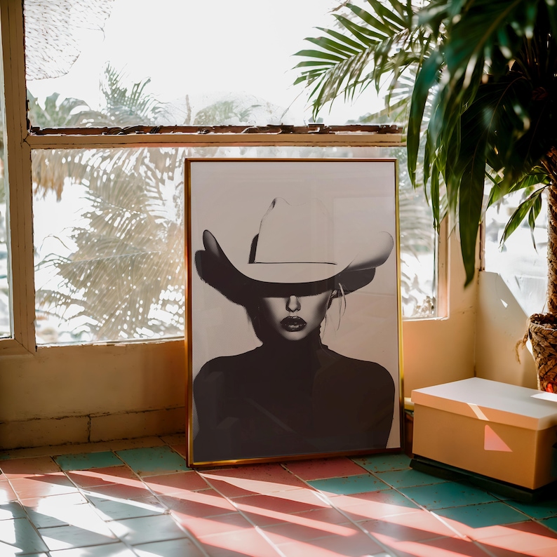 May include: A black and white photograph of a person wearing a large white cowboy hat. The person is looking directly at the camera. The photograph is framed in a gold frame.