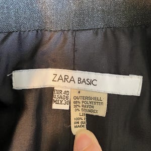 Op de afbeelding: Close-up van de voering van een donkergrijze Zara Basic blazer. Het label toont maat EUR 40, US AD8, MEX 30, en de samenstelling van de buitenkant: 65% polyester, 32% rayon en 3% spandex. De voering is 100% linnen.