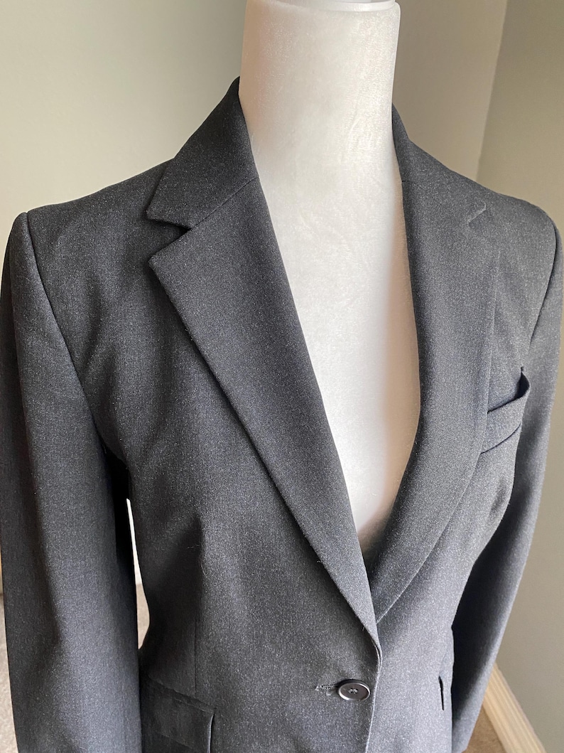 Op de afbeelding: Een antracietgrijze blazer met een revers en een sluiting met &eacute;&eacute;n knoop. De blazer heeft een getailleerde pasvorm, een borstzak en een klassiek ontwerp. De stof lijkt een geweven materiaal te zijn, geschikt voor professionele of formele kleding.