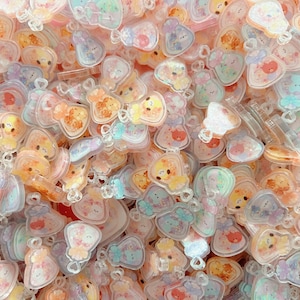 May include: A collection of pastel-colored acrylic charms with various cute animal and object designs. The charms feature a mix of pink, orange, blue, and yellow hues, with clear plastic loops for attachment. The overall theme is whimsical and playful.