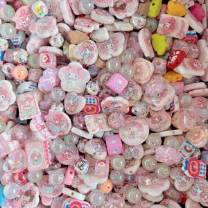 May include: A collection of pink and white beads and charms. The assortment includes various shapes, such as flowers, hearts, and squares, with cartoon character designs. Some beads are iridescent, and others are solid colors.
