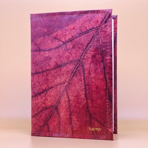 Op de afbeelding: Een bordeauxrood lederen gebonden dagboek met een bladmotief op de omslag. Het dagboek heeft een witte rug en het woord "NACTRY" is in goud op de omslag gedrukt.