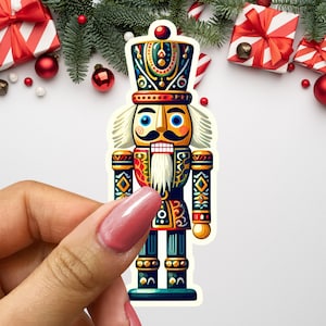 May include: A colorful nutcracker figurine with a red, green, and gold painted design. The nutcracker has a white beard and mustache, blue eyes, and a red hat with gold trim.