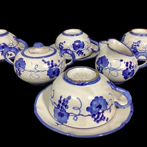 Può includere: Servizio da tè in ceramica bianca con disegni di viti d'uva blu. Il set comprende tazze, piattini, una teiera e una lattiera. I bordi e le maniglie sono dipinti di blu.