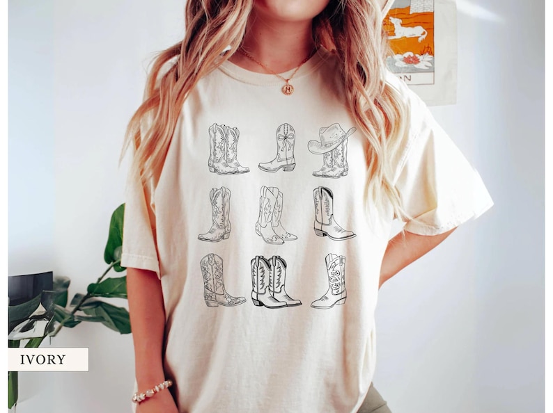 May include: Ivory-colored t-shirt featuring a collection of nine different cowboy boot designs in black line art. The boots vary in style, with some having intricate patterns and others a more classic look. The word "IVORY" is printed at the bottom.