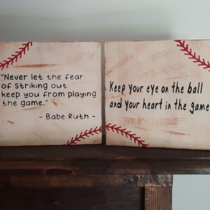 May include: Two wooden signs with baseball stitching painted on them. The left sign has a quote from Babe Ruth: "Never let the fear of striking out keep you from playing the game." The right sign says "Keep your eye on the ball and your heart in the game."