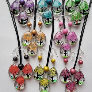 May include: A set of 10 necklaces and earrings featuring a teardrop-shaped pendant with a tree and butterflies inside. The pendants are made of clear glass and come in a variety of colors, including blue, green, purple, pink, yellow, and orange.