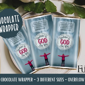 Op de afbeelding: Een blauwe en witte chocoladeverpakking met een roze en witte cirkel waarop "Grateful to God for His Blessings" staat. De verpakking bevat ook een bijbelvers uit Efeziërs 3:20.